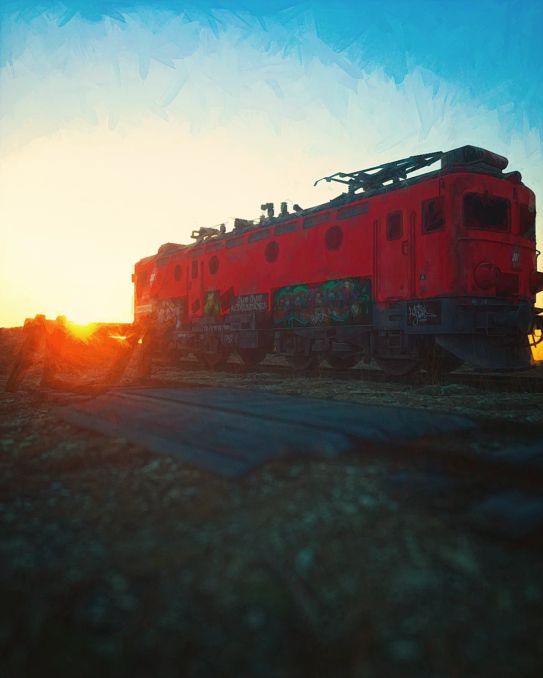 A red locomotive in a train yard at sunset.